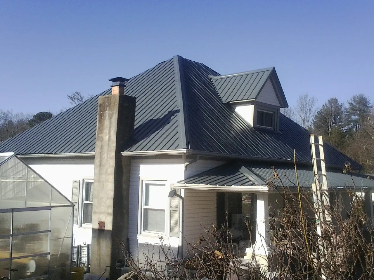 Dark blue standing seam metal roof on a white farmhouse with dormer — Slate & Tile Roof Repair by Roofing Brothers in Newburg