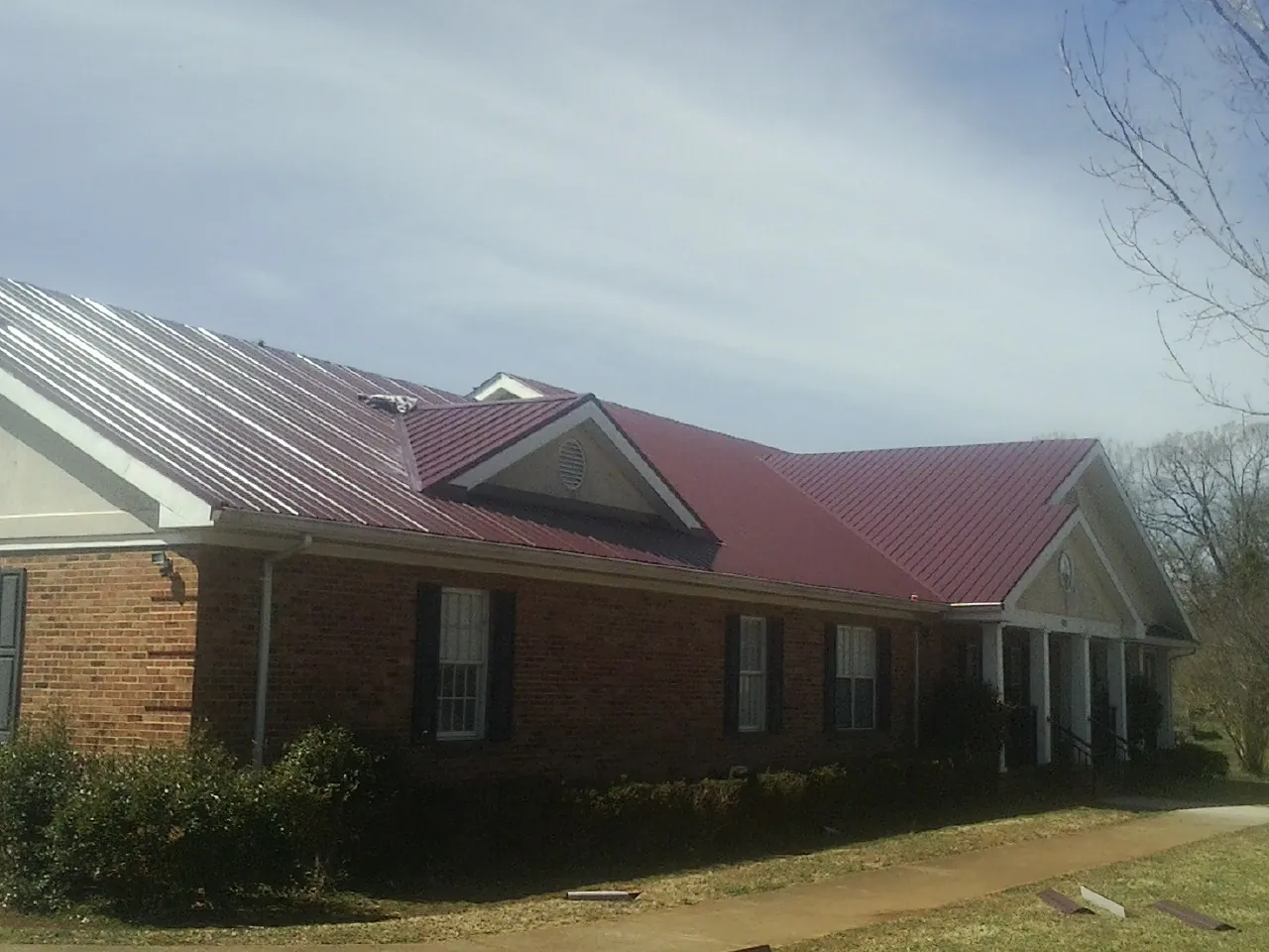 Red metal roof with gabled entries on a long brick building, from a Hail Damage Roof Repair job in Newburg
