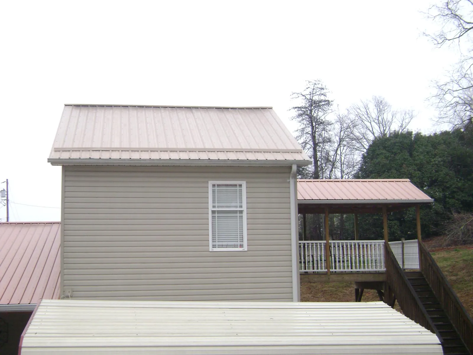 Tan metal roofs on a two story addition and attached porch, from a Roof Replacement job in Newburg